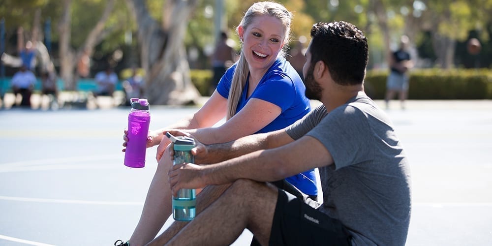 Brand Ambassadors, Stacey and Richard talking and drinking water on a basketball court.