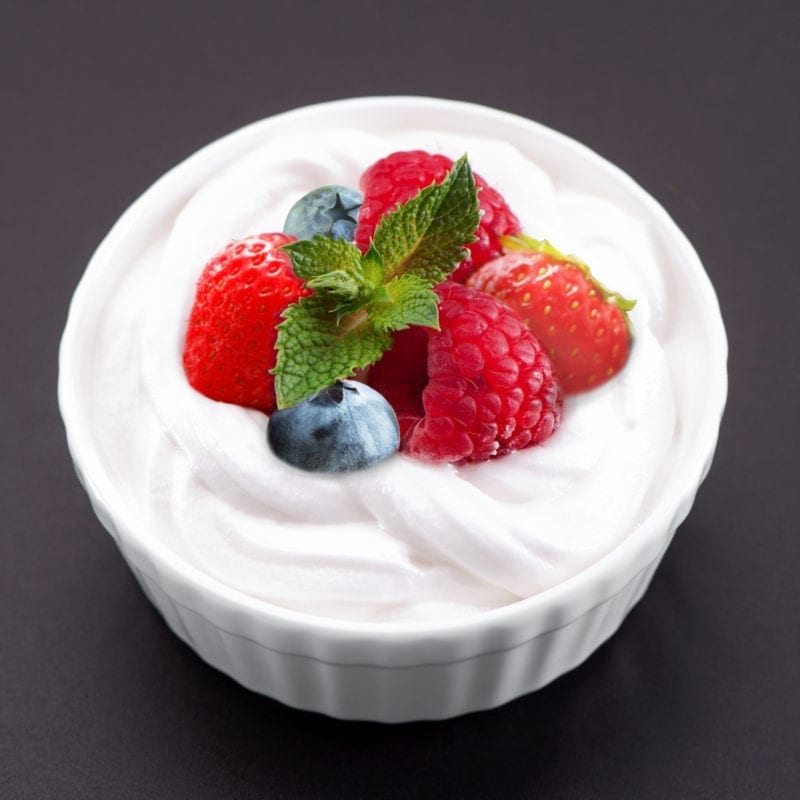 Cheesecake dip topped with raspberries, strawberries, blueberries, and mint in a white ramekin.