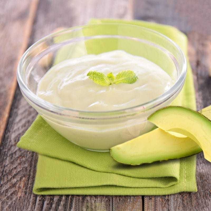 Vanilla pudding in a clear bowl sitting on a green napkin with avocado slices on the side.