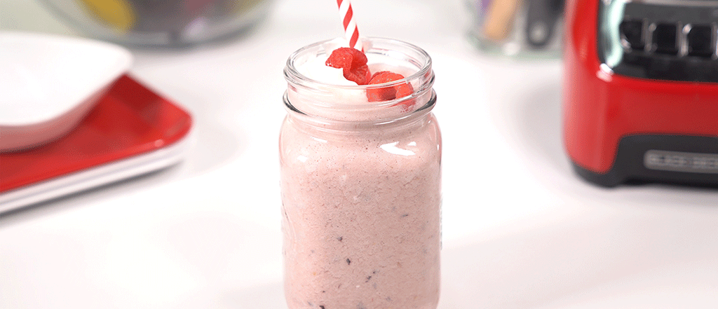 Sugarplum Smoothie in a mason jar with a red and white straw and topped with raspberries.
