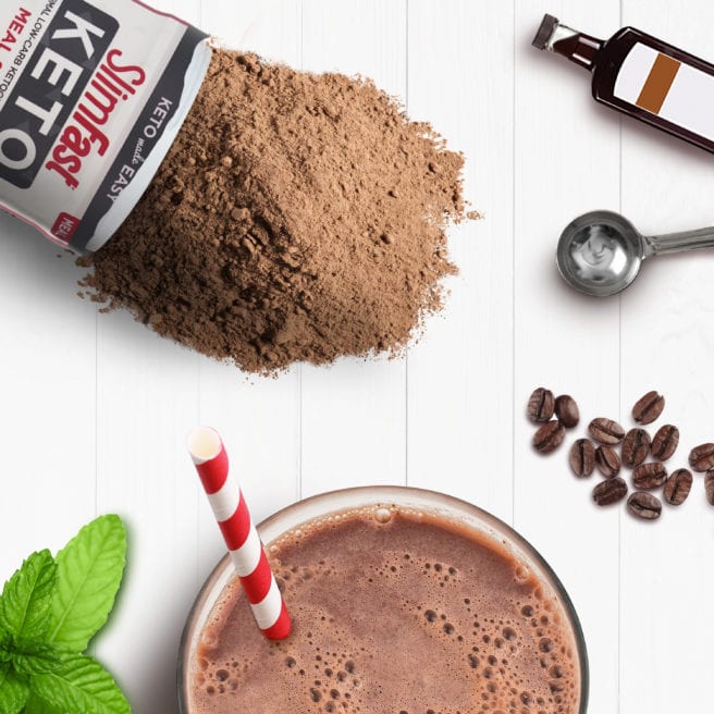 SlimFast Keto shake accented with spilled Keto Fudge Brownie Batter Shake Mix, extract bottle, mint leaves & coffee beans