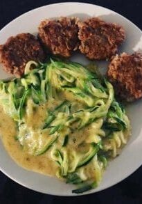 Zucchini noodles with yellow sauce and turkey meatballs on a white plate.